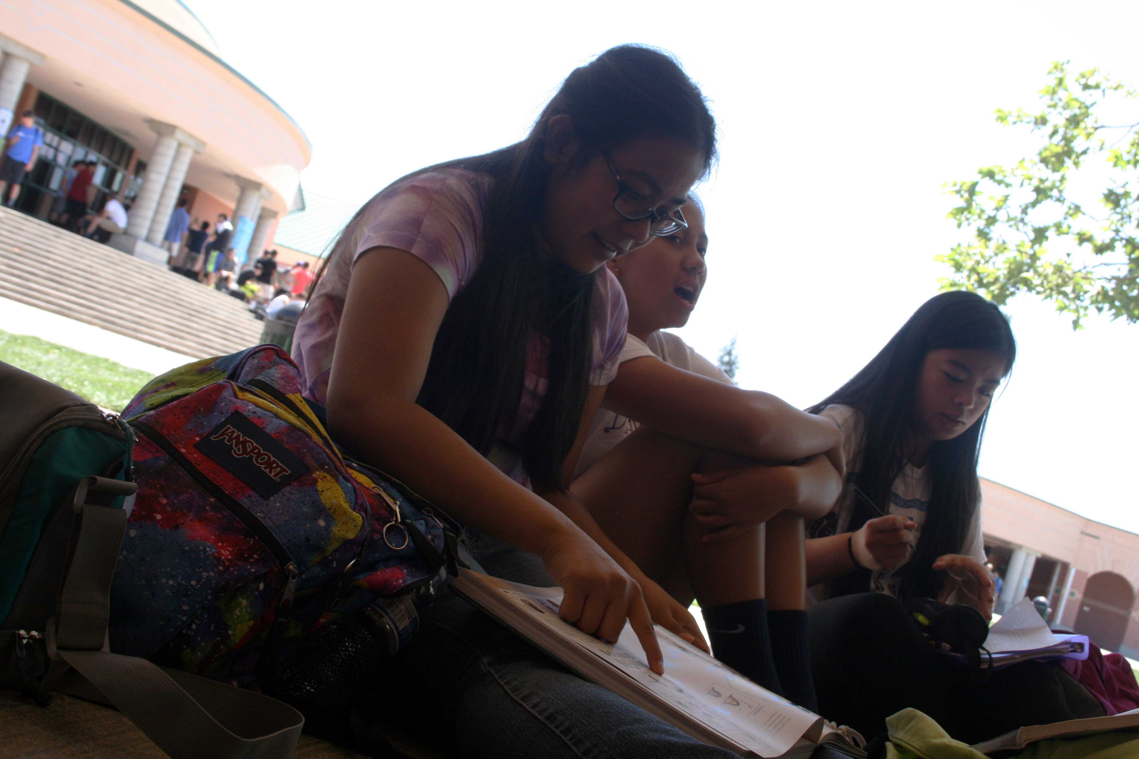 To show her friends, freshman Sarah Ansari points at a drawing in her book during second lunch on April 16. The book was called High Rule Historia and she brought it to school so she could share it with her friends. “I like that the book has lots of concept art and it has Legend of Zelda in it,” Ansari said. Photo by Nishita Fernandes