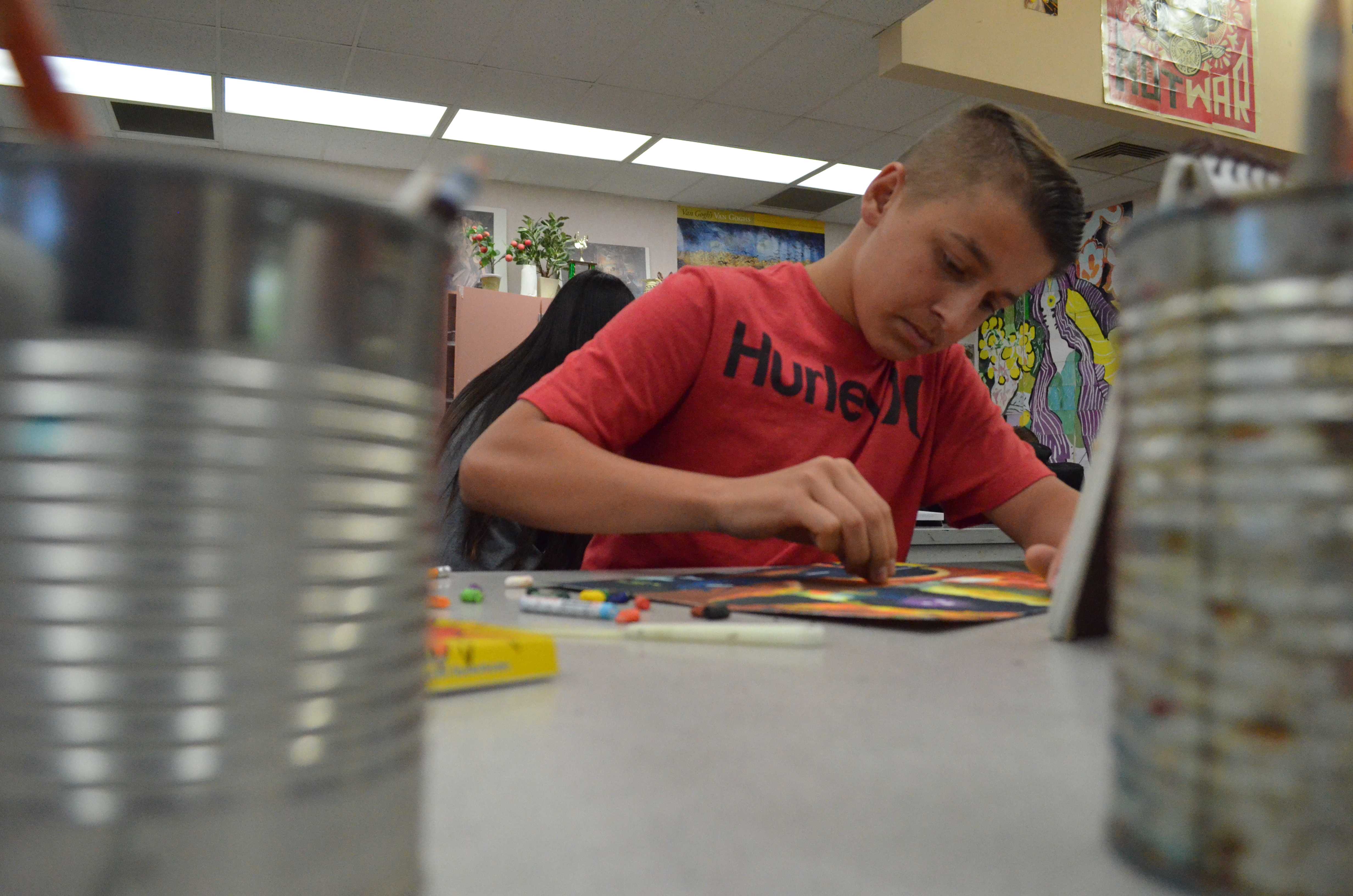SHARPER FOCUS: Although other students laughed and talked with one another, freshman Matt Dulong kept his head down to work on his pastel project. Each student chose individual and personal pictures to create artwork that meant something to them. Dulong’s piece depicted a man standing in a boat, fishing underneath a bridge. “For my project I decided to incorporate my grandfather. He was a fisherman, so I am trying to capture that memory I have of him,” Dulong said. Photo by Michaelan George